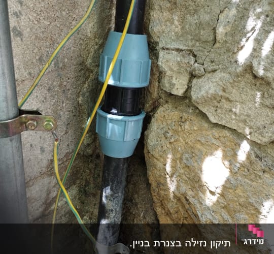 צינור מים עם מחברים כחולים על קיר אבן